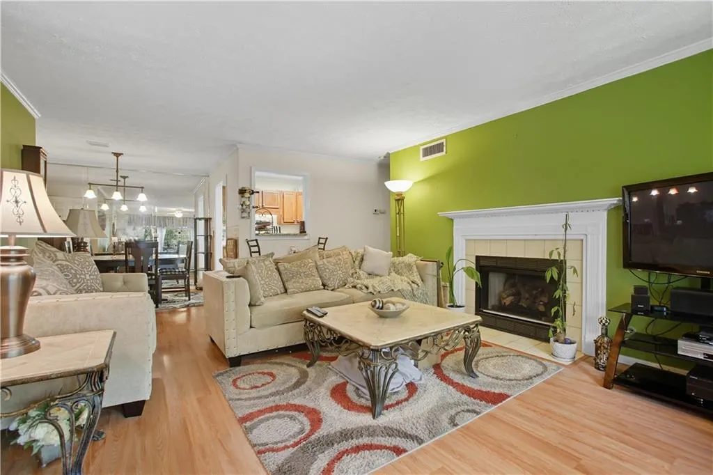 Living room with wood finished floors, a tiled fireplace, and ornamental molding