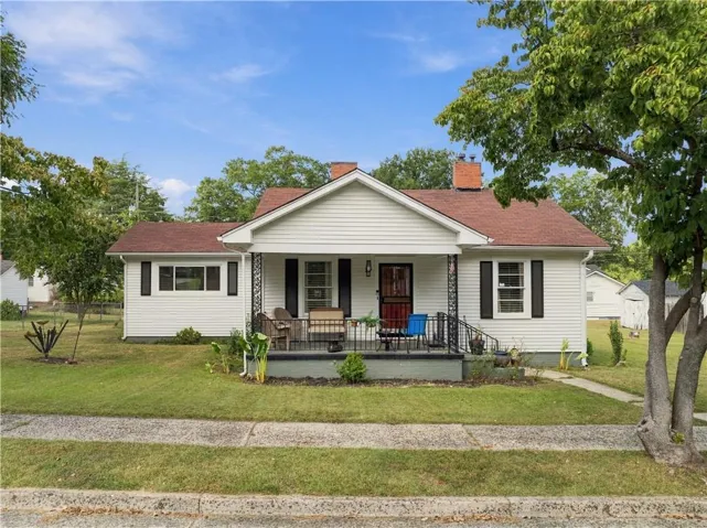 White siding exterior with black window shutters, a covered front porch, and a red shingle roof