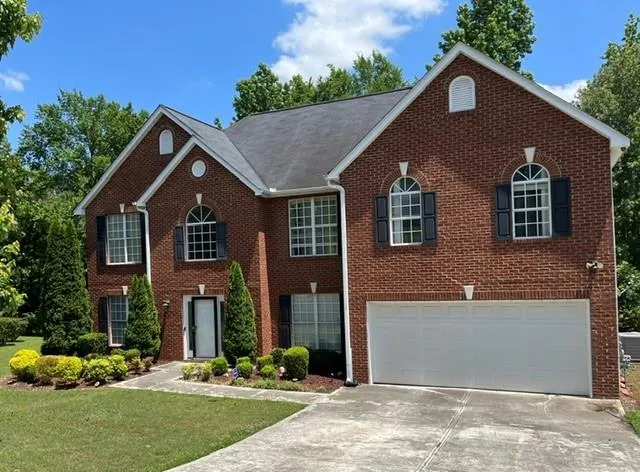 Traditional brick exterior with white trim, featuring a two-car garage, manicured shrubs, and a concrete driveway