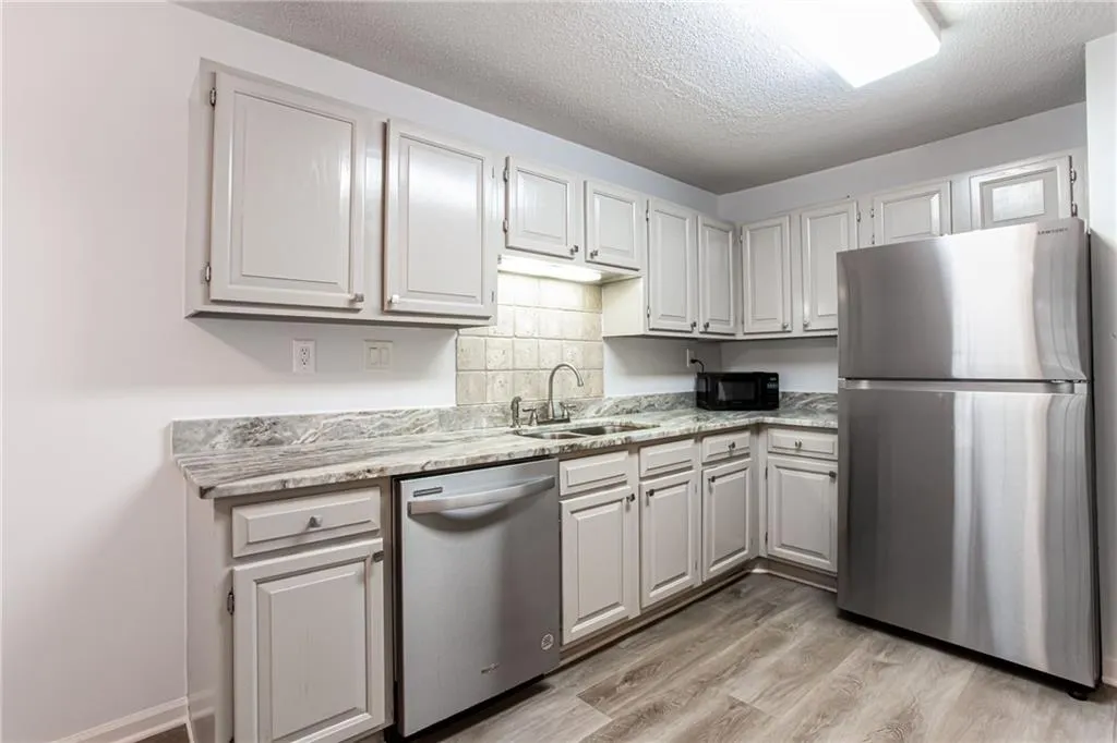 Kitchen with appliances with stainless steel finishes, tasteful backsplash, a textured ceiling, light wood-style floors, and light stone counters