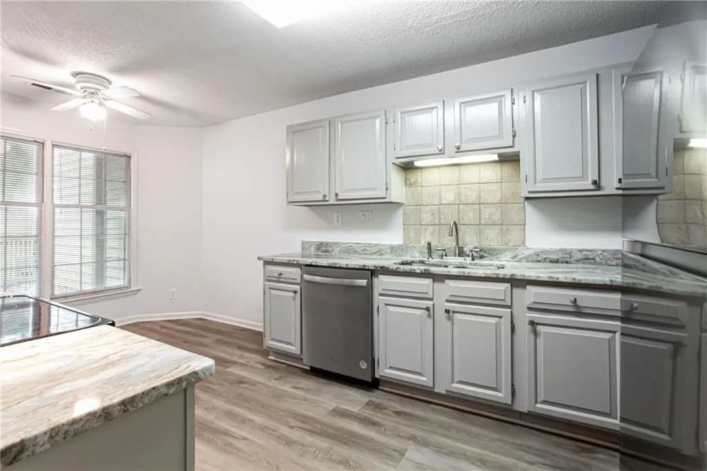 Kitchen with gray cabinetry, decorative backsplash, light wood finished floors, dishwasher, and a ceiling fan