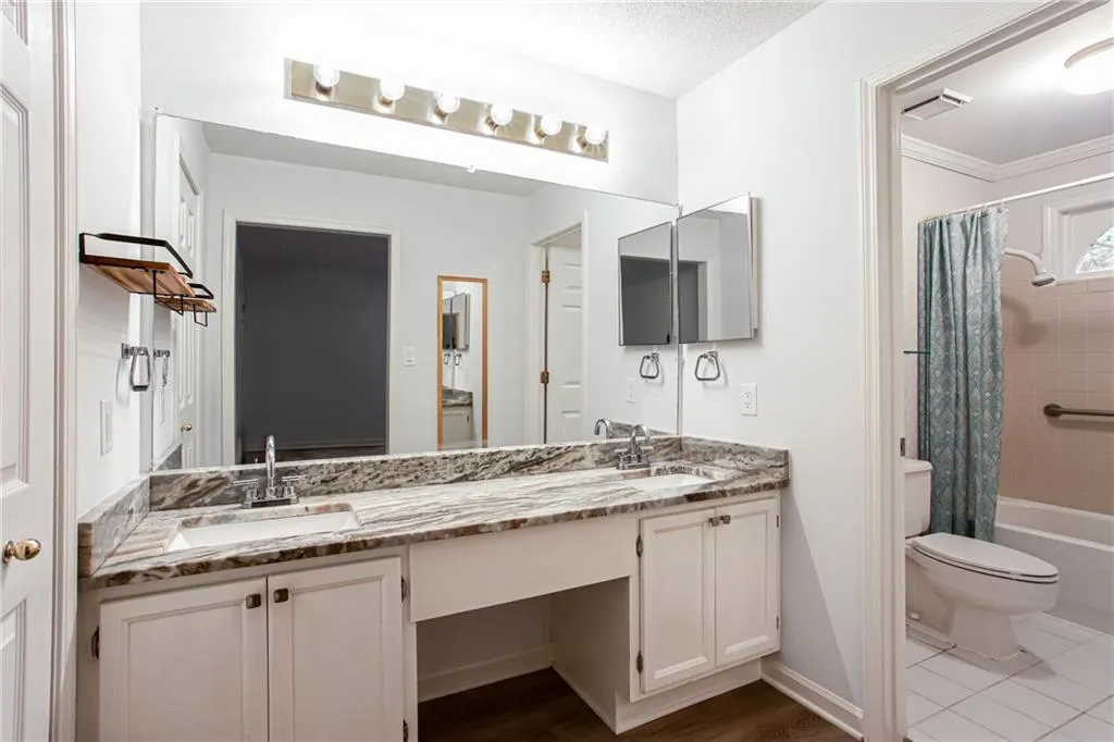 Bathroom featuring shower / bath combo with shower curtain, double vanity, a textured ceiling, ornamental molding, and dark wood-style flooring