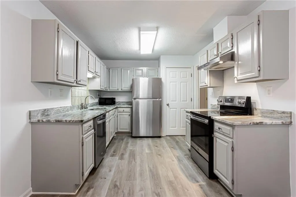 Kitchen with appliances with stainless steel finishes, light wood finished floors, under cabinet range hood, light stone countertops, and a textured ceiling