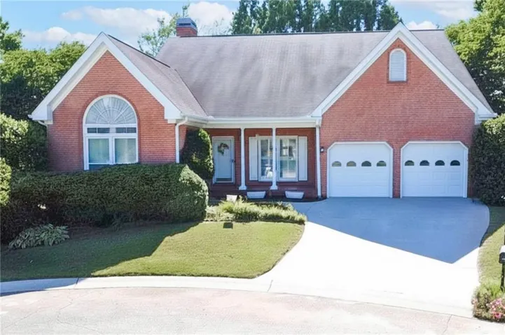 Brick exterior with white trim, arched window, covered porch entry, two-car garage, and a concrete driveway