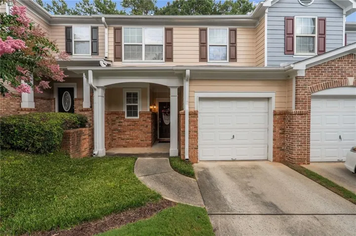 Townhome exterior featuring brick and siding construction, covered entry, attached single-car garage, and established landscaping