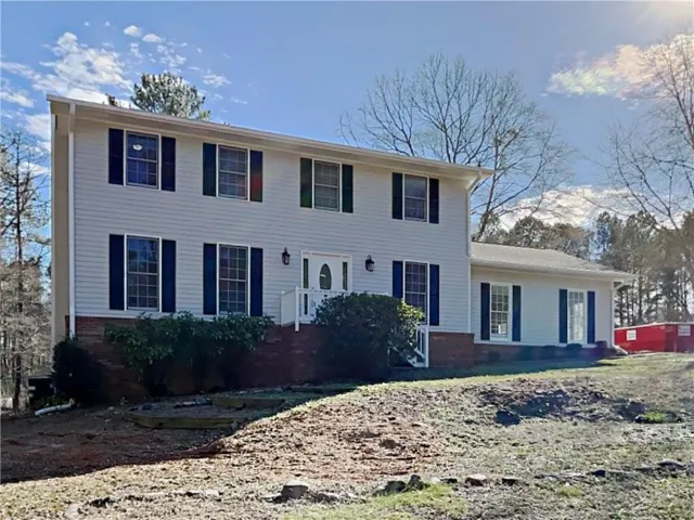 Traditional two-story residence featuring white siding, dark shutters, a brick foundation, and a partial front porch with railings