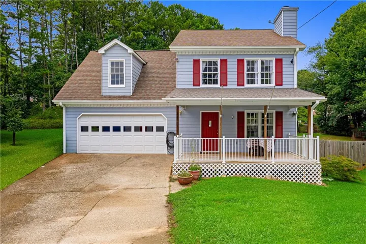 Light blue siding exterior with red shutters, a dormer window, an attached garage, a full front porch with white railing, and a concrete driveway