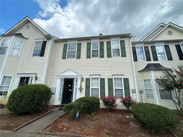 Exterior, front view featuring decorative shutters in green and a black door, a stone-edged walkway, and established foundation plantings with blooming roses