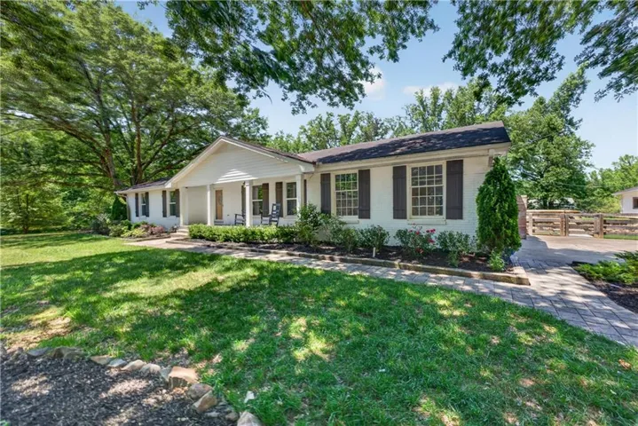 Charming traditional ranch residence with a classic front-facing design, featuring a covered front porch with columns, black shutters framing large windows, and light-colored exterior brick and siding