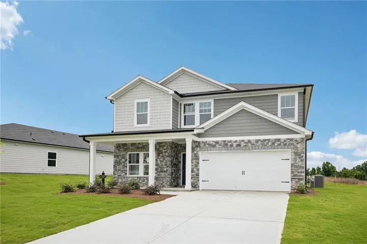 Two-story residence featuring a stone and siding facade, a covered front porch with columns, a two-car garage with white doors, multiple windows with white trim, and a concrete driveway
