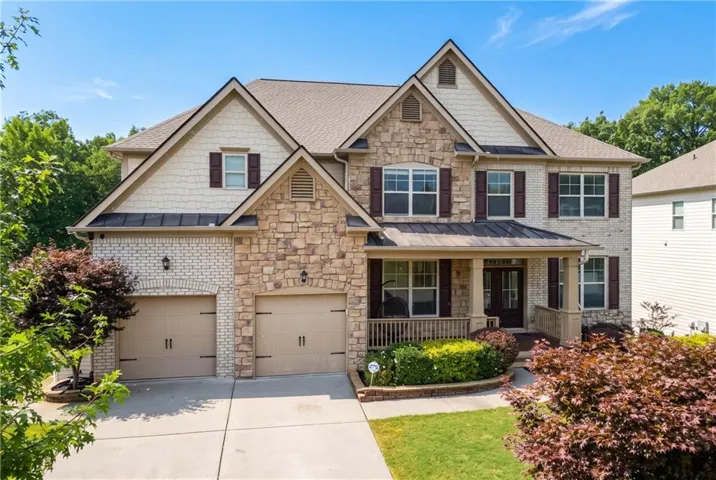 Multi-level residence featuring a stone and brick facade, two-car garage, and covered front porch with columns