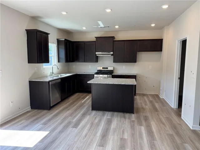 Modern kitchen featuring dark cabinetry with stainless steel appliances, white subway tile backsplash, light wood-finish flooring, recessed ceiling lighting, and a centered island with contrasting countertop