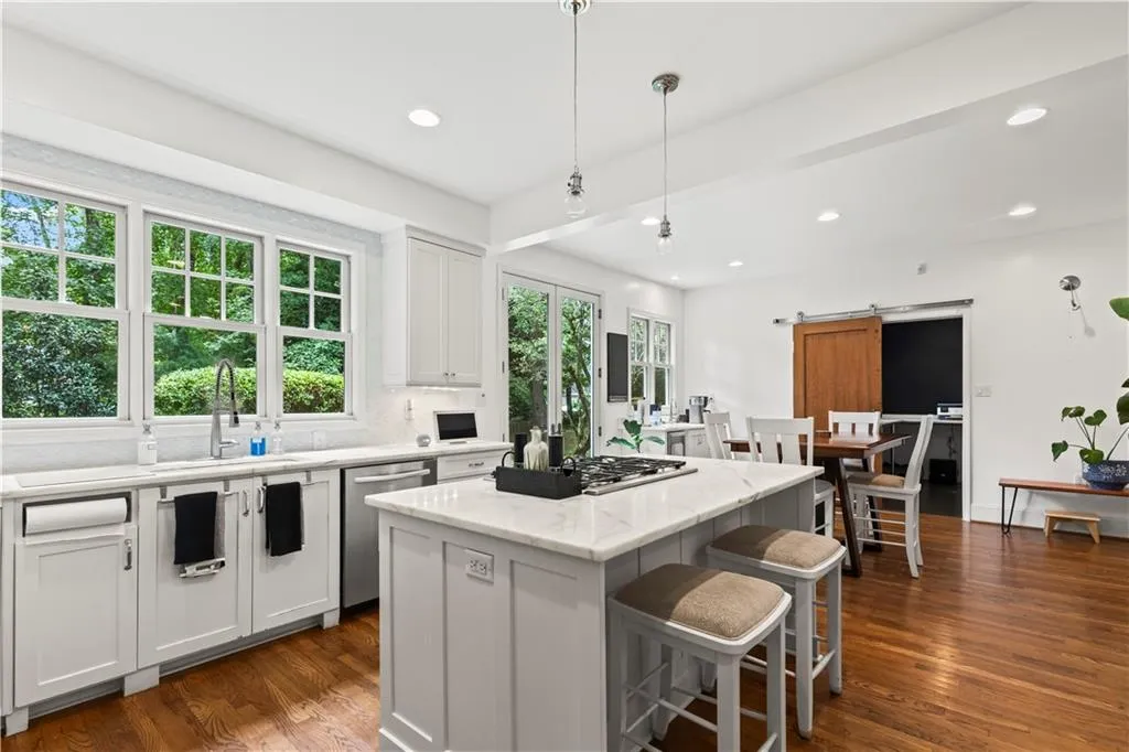 Kitchen with a barn door, white cabinetry, light stone countertops, pendant lighting, and dark wood-type flooring