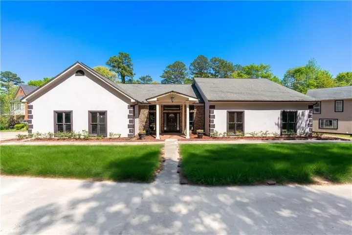 Single-story residence featuring a central covered entry, stucco exterior with stone accents, dark window trim, a gabled roofline, and a concrete walkway