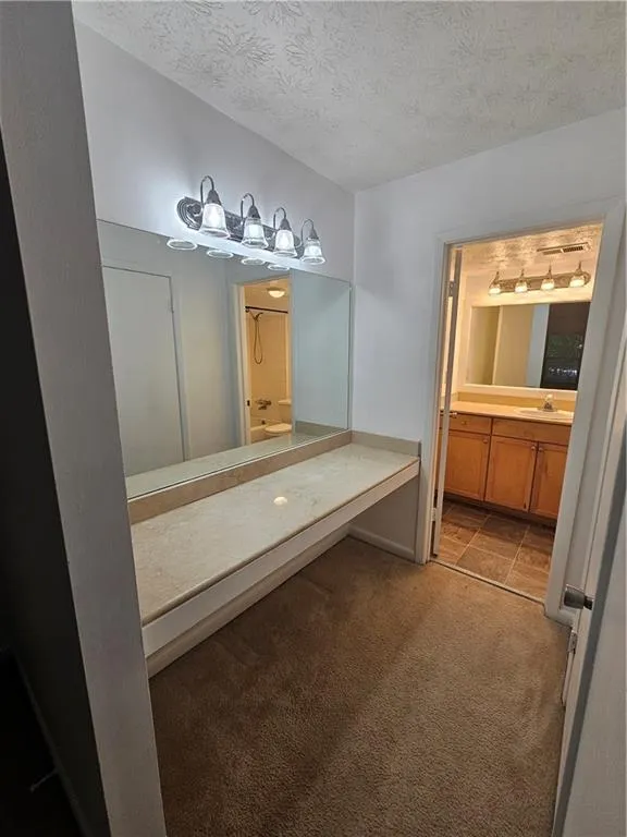 Full bath featuring a textured ceiling, vanity, carpet, and a shower