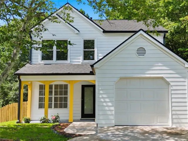 White two-story residence featuring a single-car garage with a panel door, a covered entry with yellow support pillars, and a black-framed front door with decorative glass
