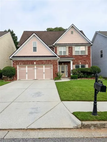 Brick facade with light-colored siding accents, dual garage doors, a concrete driveway, and a front lawn with foundational shrubs