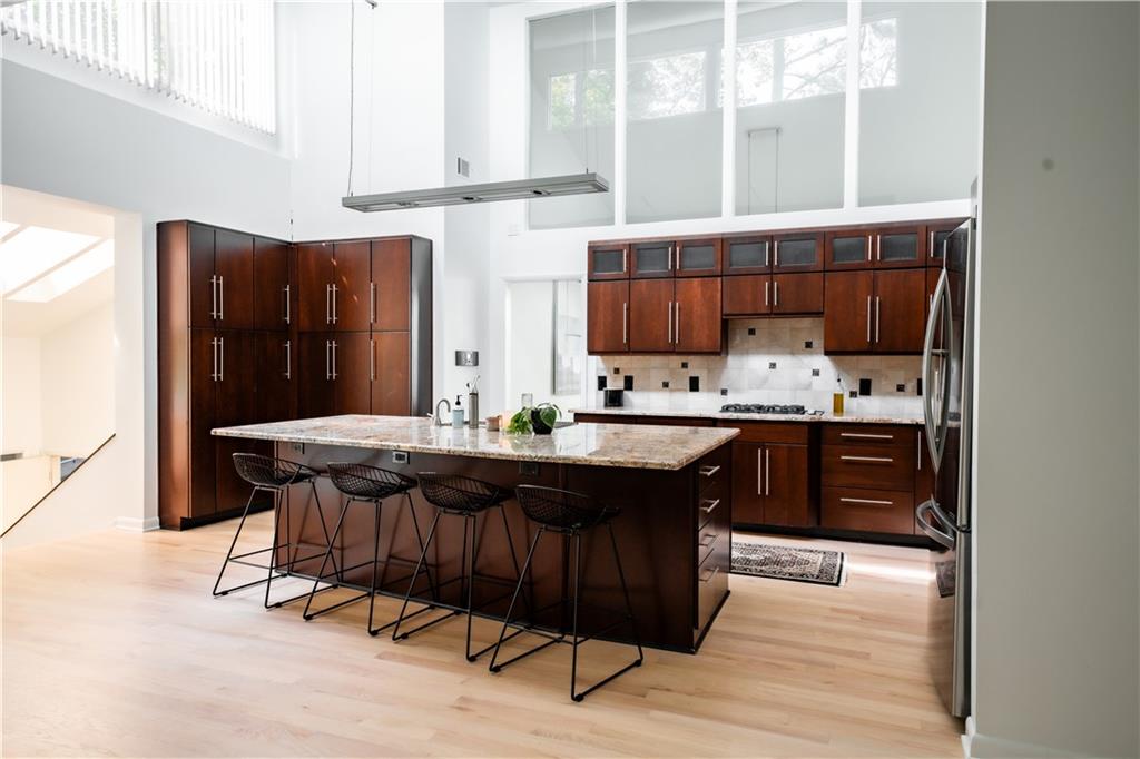 Kitchen featuring a towering ceiling, island exhaust hood, a kitchen bar, light hardwood / wood-style flooring, and a center island with sink