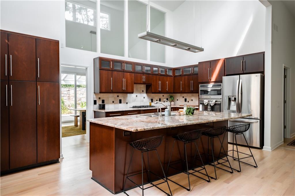Kitchen with a towering ceiling, a kitchen breakfast bar, stainless steel appliances, light stone counters, and light wood-type flooring