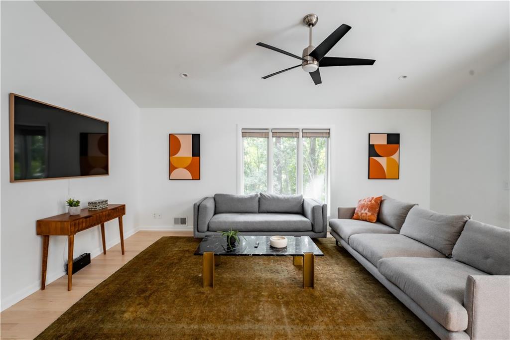 Living room with light hardwood / wood-style floors, lofted ceiling, and ceiling fan