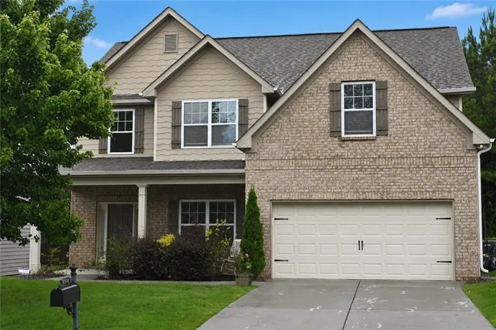 Two-story residence featuring a brick and siding facade, a two-car garage, and a covered front porch with columns