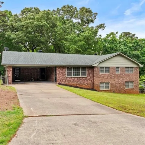 Brick exterior with a gray shingle roof, featuring a two-car carport, a concrete driveway, and a sloped lawn