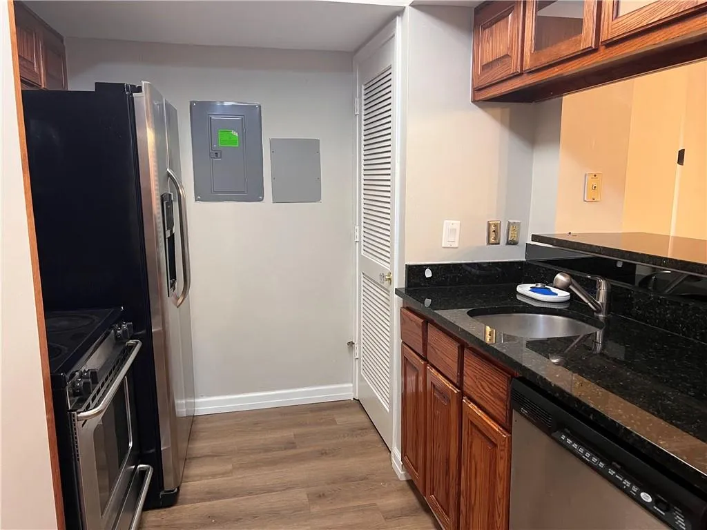 Kitchen with brown cabinetry, stainless steel appliances, electric panel, and wood finished floors