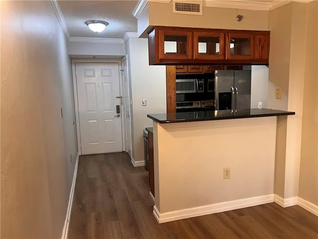 Kitchen with crown molding, stainless steel appliances, dark wood-style flooring, dark countertops, and a peninsula