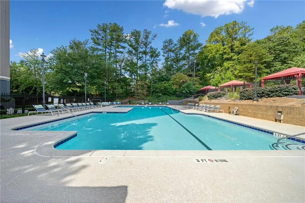 Community pool with a patio area and view of wooded area