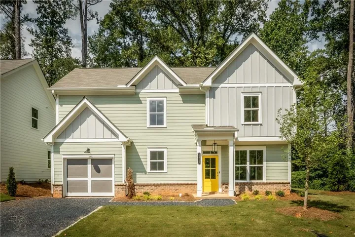 View of front facade with board and batten siding, a front yard, driveway, and brick siding