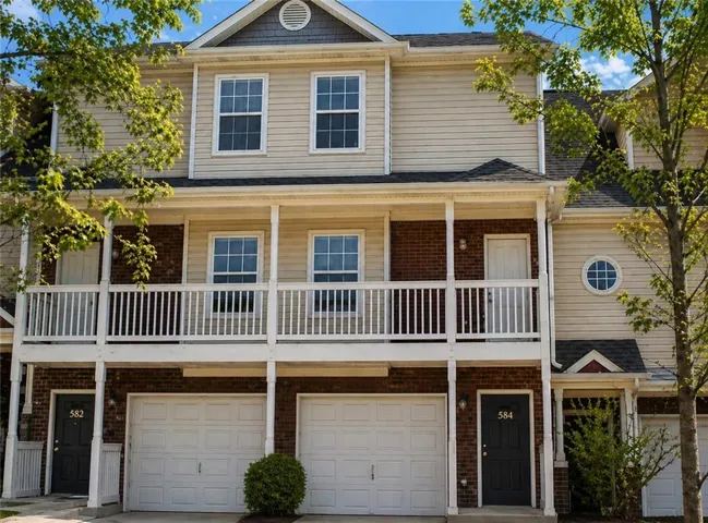 Multi-level townhome featuring a brick and siding exterior, white railing balcony, and individual garage doors