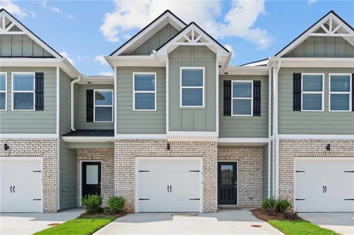Townhome facade featuring light green siding, white brick, black shutters, and white garage doors