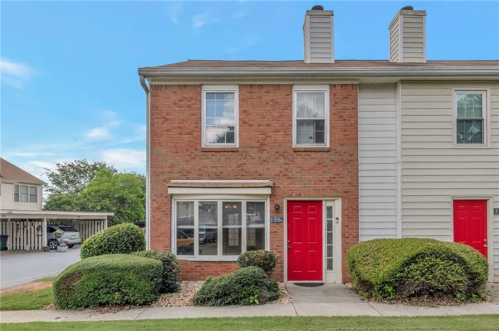 Brick facade, bay window, red entry door, dual chimneys, and mature landscaping