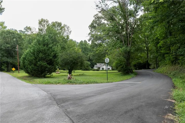 Paved road intersection with a white house in the background, set amidst a verdant landscape