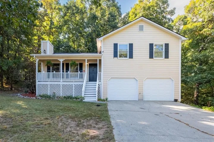 Two-car garage, covered porch with white railing, light-colored siding, and dark shutters