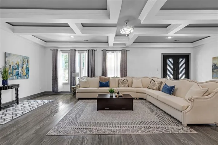 Spacious room featuring wood-finish flooring, coffered ceilings with recessed lighting, a decorative chandelier, and tall windows