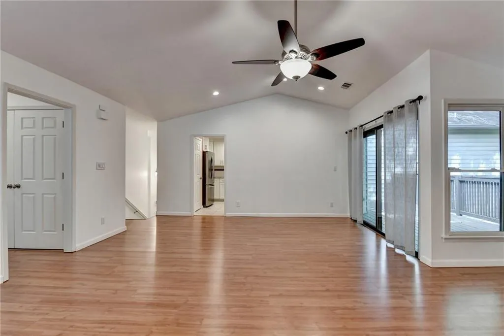 Unfurnished living room with ceiling fan, light wood-type flooring, visible vents, baseboards, and lofted ceiling