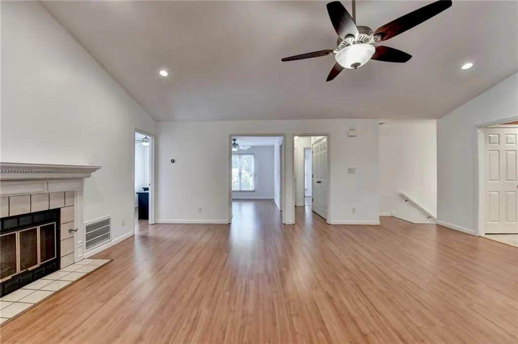 Unfurnished living room with visible vents, vaulted ceiling, wood finished floors, a tiled fireplace, and a ceiling fan