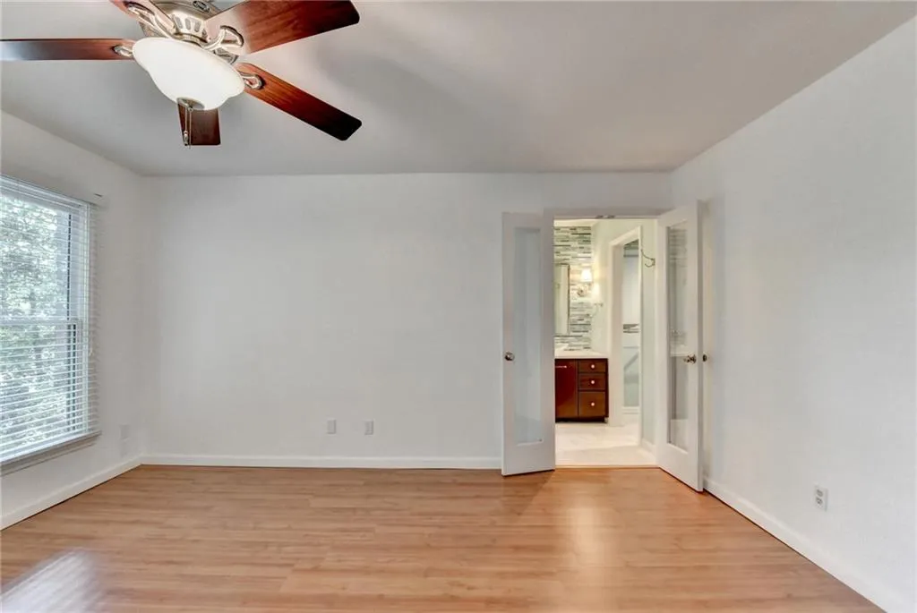 Unfurnished bedroom featuring ensuite bath, a ceiling fan, light wood finished floors, and baseboards