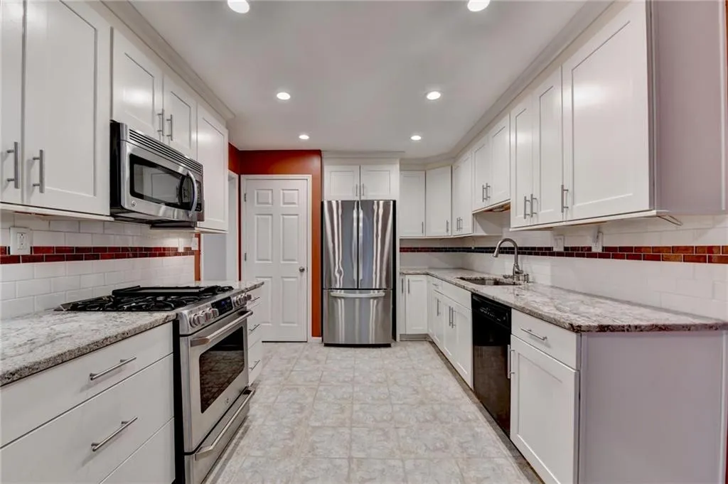 Kitchen with backsplash, a sink, light stone counters, and appliances with stainless steel finishes