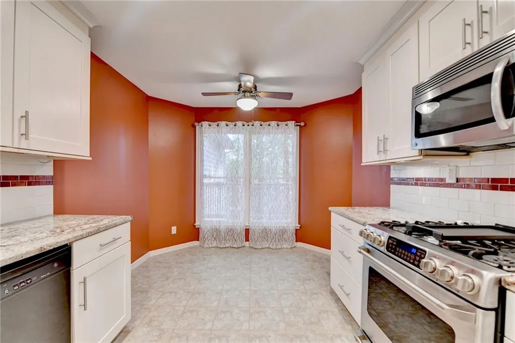 Kitchen featuring appliances with stainless steel finishes, ceiling fan, white cabinetry, and baseboards