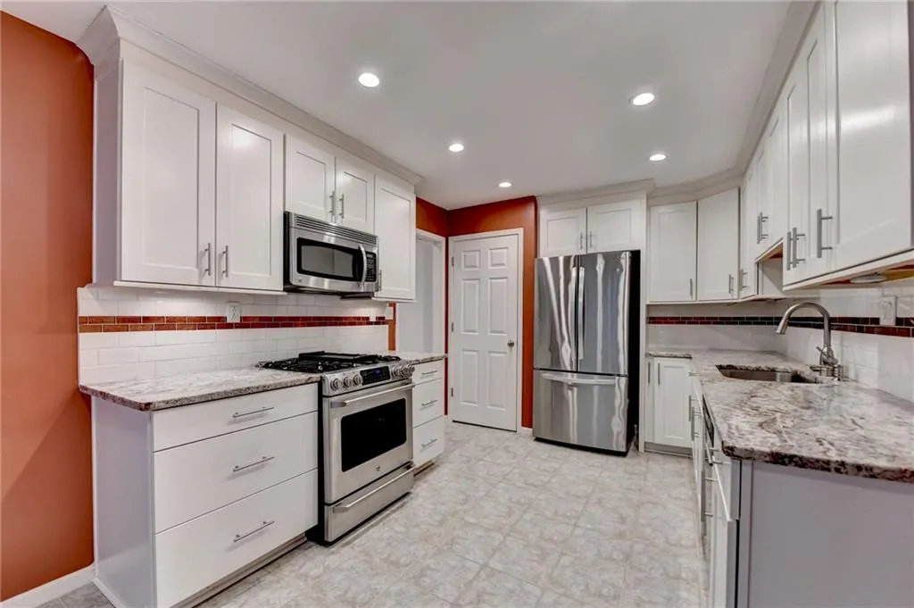 Kitchen with light stone countertops, stainless steel appliances, backsplash, and a sink