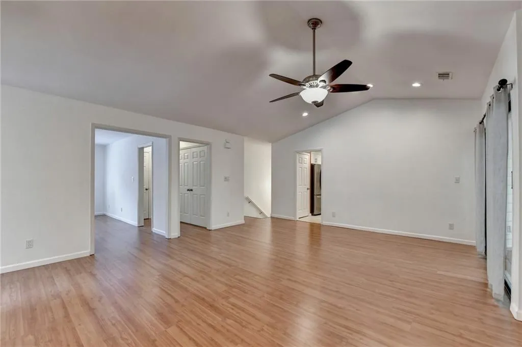 Unfurnished living room featuring light wood-style flooring, a barn door, visible vents, a ceiling fan, and lofted ceiling