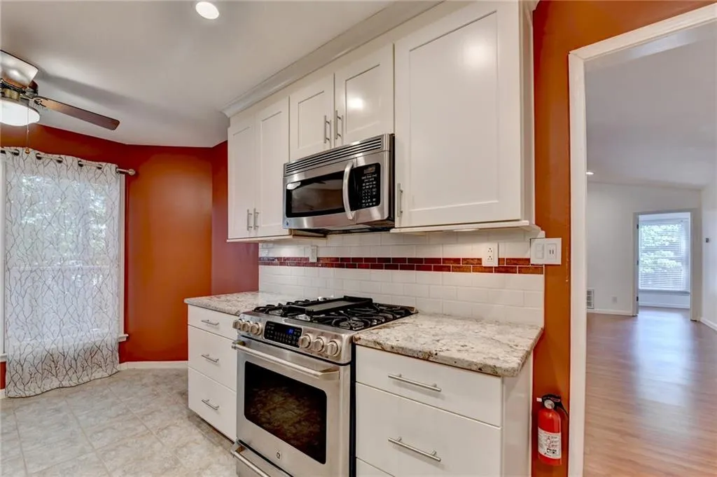 Kitchen featuring appliances with stainless steel finishes, decorative backsplash, a ceiling fan, and white cabinets