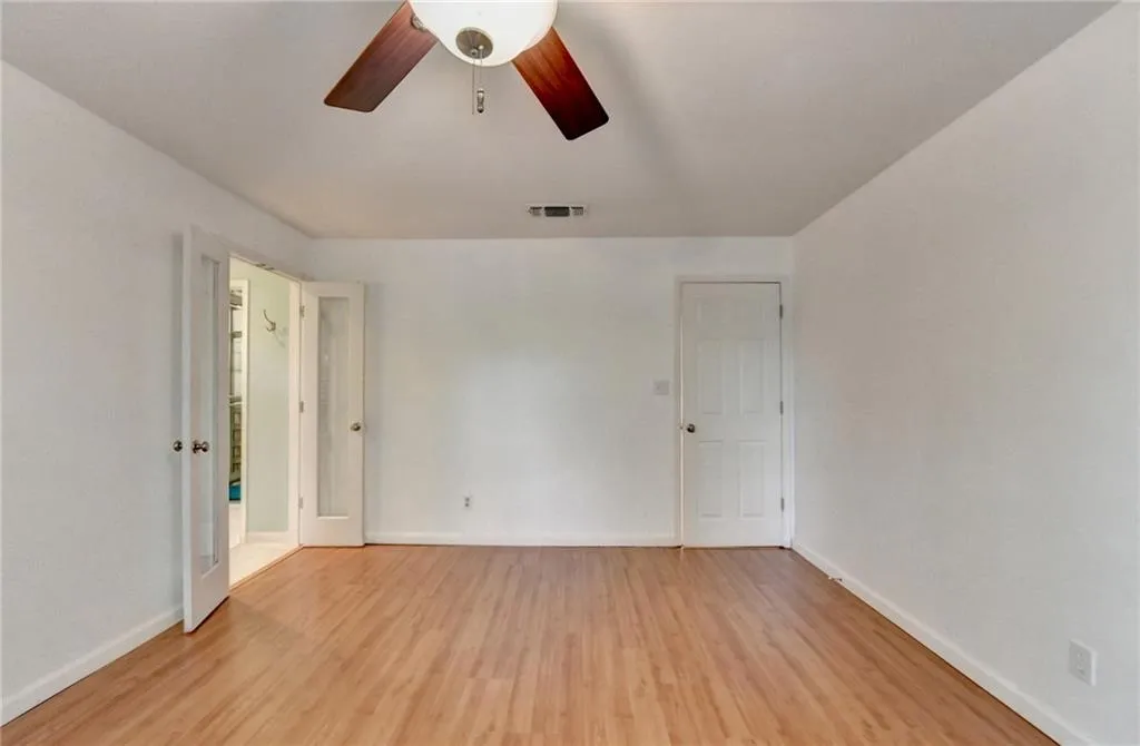 Empty room with baseboards, visible vents, ceiling fan, and light wood-type flooring