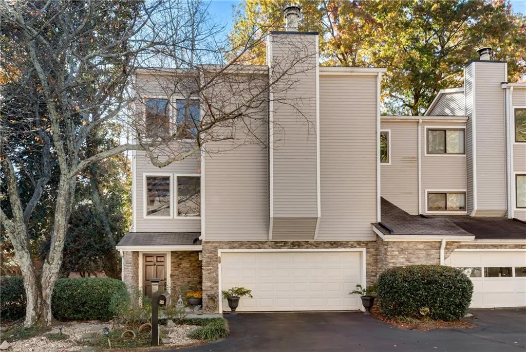 View of front of property featuring stone siding, driveway, a chimney, and an attached garage