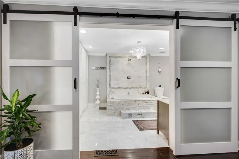 NEW Double Sliding Doors open to a View of the Luxuriously Updated Carrera Marble & Split Stone Primary Bath.
