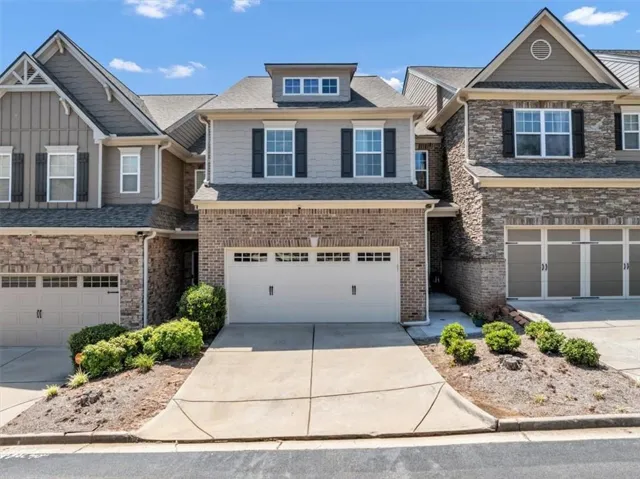 Townhome exterior featuring a two-car garage with a concrete driveway, brick and siding facade, dormer windows, and black louvered shutters