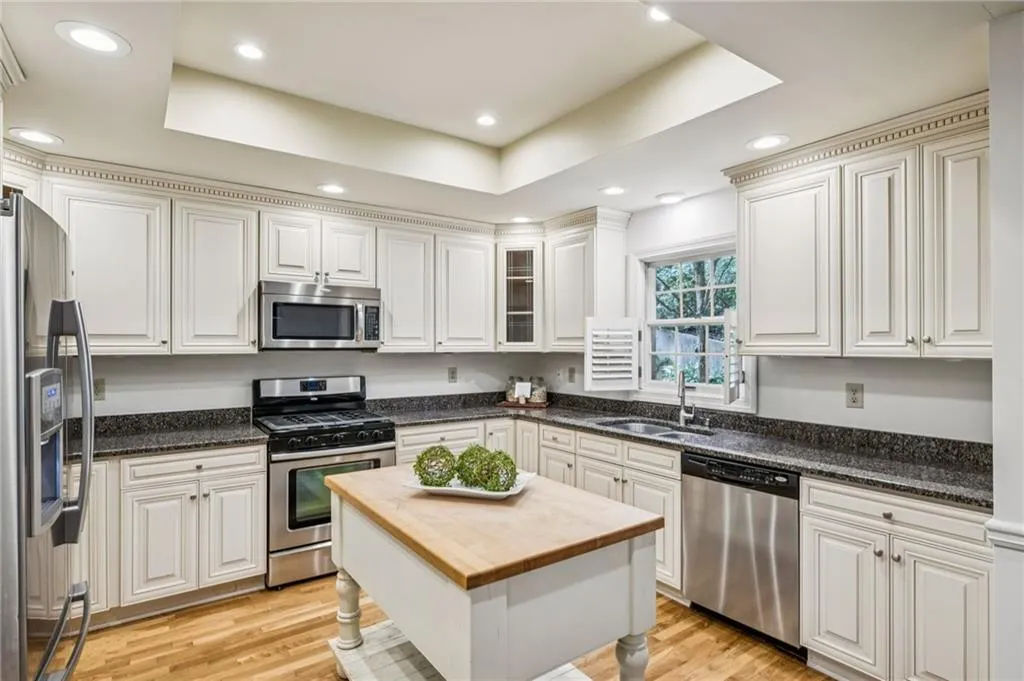 Kitchen with stainless steel appliances, dark stone countertops, a tray ceiling, light wood-style flooring, and recessed lighting