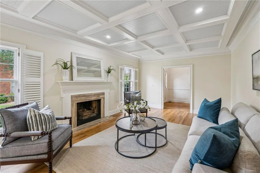 Living room with beamed ceiling, light wood-type flooring, coffered ceiling, a fireplace, and crown molding